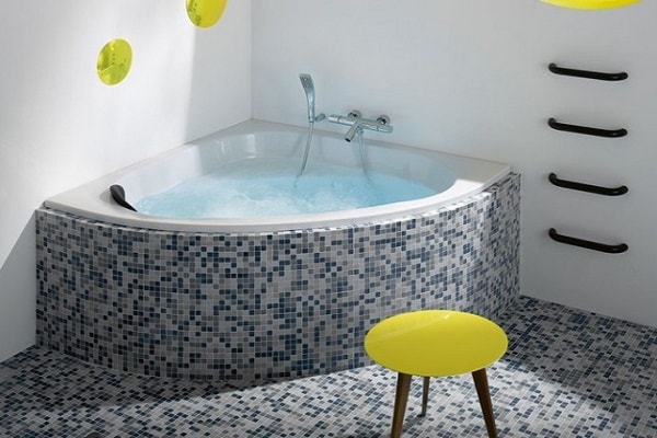 Une baignoire d'angle signée Jacob Delafon avec mosaïque faïence grise et bleue.