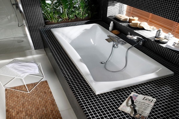 Une petite baignoire encastrée dans une salle de bain avec faïence noire.