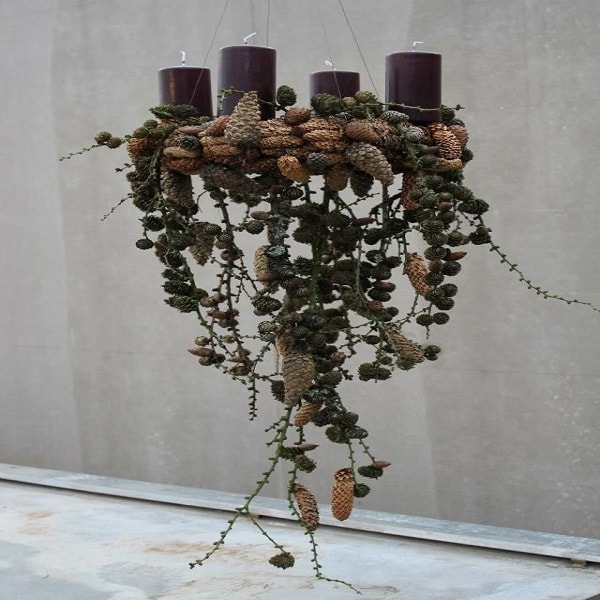 Une suspension qui met en valeur des bougies sur un lit d'éléments végétaux en tous genres pour une déco Noël contemporaine.