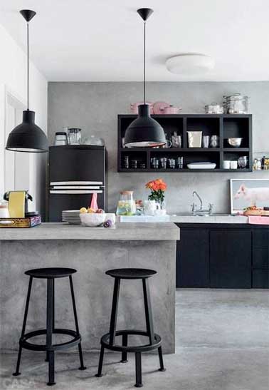 L'aspect doux du béton ciré indus sur le carrelage du sol et des murs de la cuisine ouverte s'harmonise avec l'électroménager et le mobilier en bois noir mat. 
