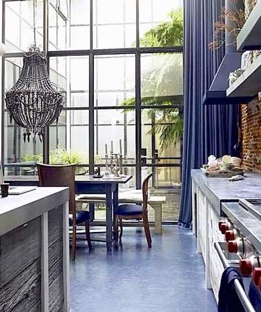 Cuisine en béton ciré gris taupe et couleur bleu s'associent dans cette pièce industrielle. Mur en brique rouge, lustre baroque gris et îlot alu font la déco