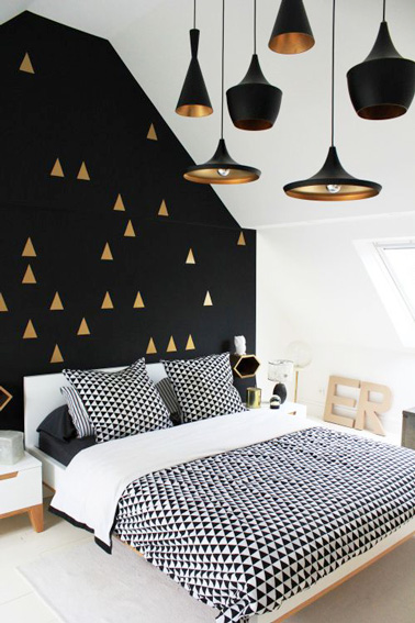 Du doré et du noir pour cette belle chambre d’amis aménagée sous les combles ! Une pièce à la déco originale avec ses lampes suspendues et ses triangles dorés. 