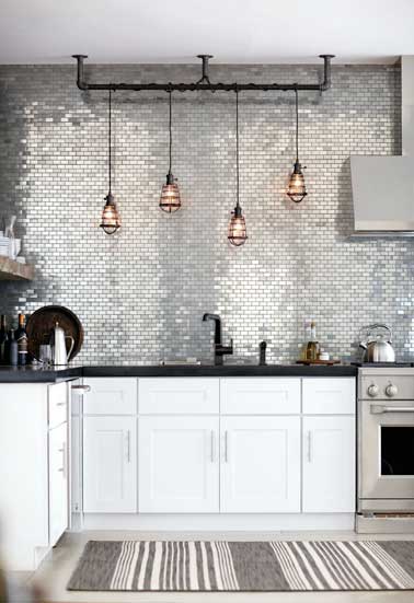 Déco de crédence en carreaux aluminium brillant pour relooker la cuisine grise. Plan de travail en pierre noir et électroménager en alu brossé donnent le ton.
