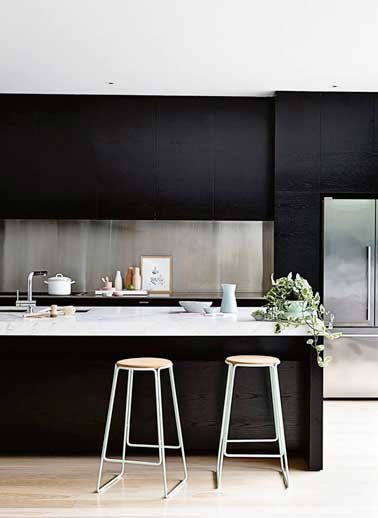 Une crédence en alu brossé installe la déco design de cette cuisine noire. Elle prend toute sa valeur placée entre des meubles de rangement en bois noir.