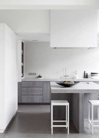 Graphique la cuisine grise se marie avec du blanc sur les murs, les meubles et les tabourets design. Nuance de gris avec le plan de travail et l'îlot en pierre 