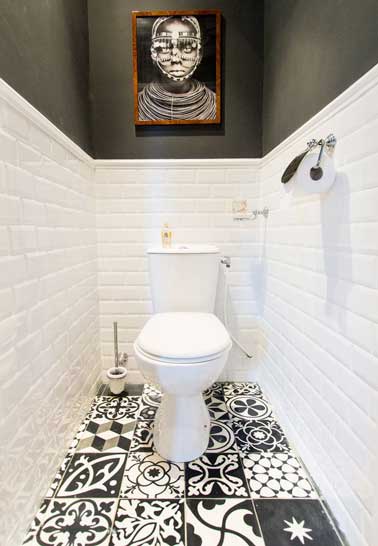 Inspiration arty dans ces toilettes à la déco noir et blanc graphique. Les murs en carrelage blanc et les carreaux de ciments imprimés au sol créent un camaïeux réussi.