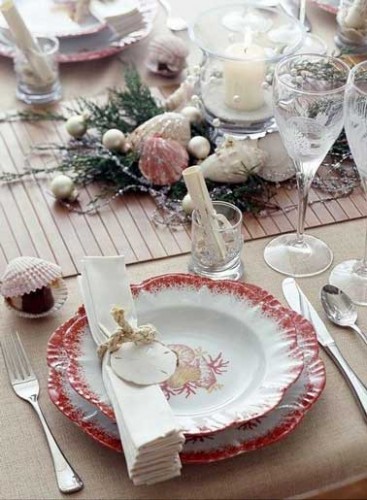 Table de Noël aux couleurs rouge et rose corail pour cette déco mer. Centre de table composé de coquillages décoratifs, de perles de mer et d'algues.
