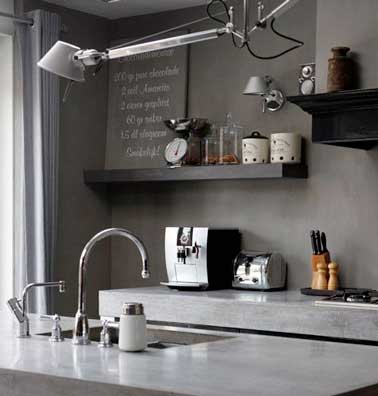Une cuisine grise 100% industrielle avec du béton ciré taupe sur les murs. Le plan de travail et l'évier en pierre brillante éclairent les nuances de gris