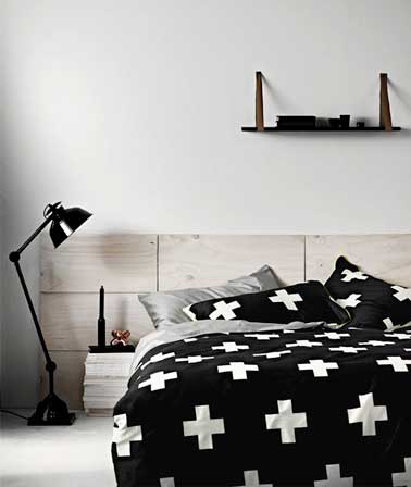 Déco graphique pour tête de lit réalisée en panneaux de bois clair blanchi. Mise en valeur par le ton noir du linge de lit et de la lampe articulé design.