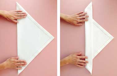 Avec une serviette dans un tissu épais, commencez le pliage de votre serviette de Noël. En deux étapes vous créez un triangle pour former la future chandelle