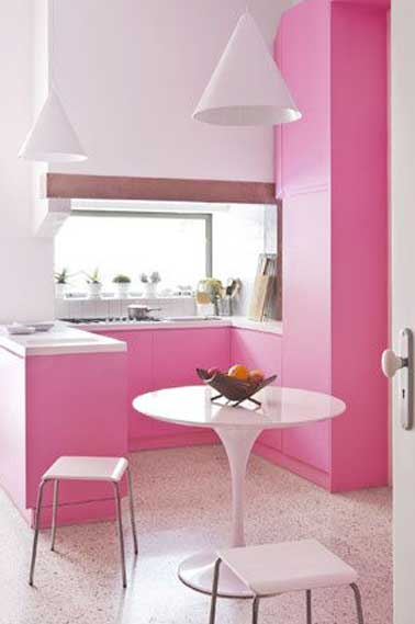 Déco de petite cuisine rose et blanc à croquer. Les meubles de rangement fuschia et la fenêtre lumineuse sur la crédence apportent profondeur à la cuisine.