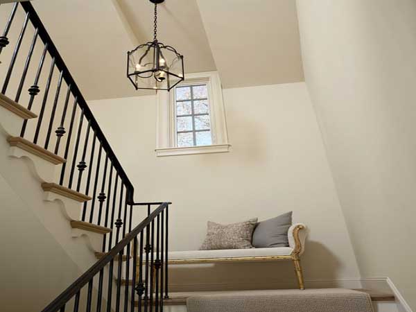 Le palier d’un escalier blanc est sublimé avec une banquette rétro. Une installation en harmonie avec les murs en peinture crème et la rampe d’escalier en fer noir. 
