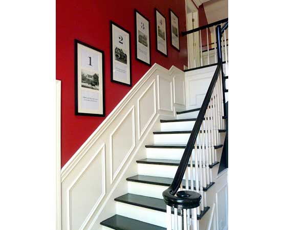 Cage d’escalier blanc style contemporain avec une peinture rouge vif sur les murs. Cadres photos en bois, rampe et marches peints en noir, ajoutent une note graphique
