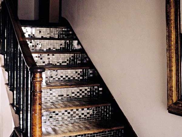 Du carrelage adhésif miroirs posés sur les contres marches de l’escalier en bois éclaire une cage d’escalier. Ici marié avec des murs peints en couleur blanc cassé