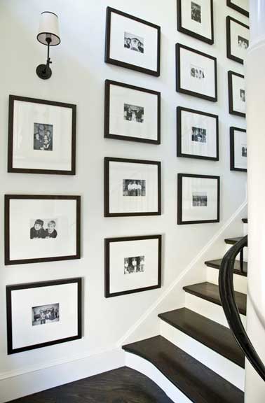 Des cadres photos en bois noirs graphiques décorent le mur de l'escalier. Un look design parfaitement associé aux tons noirs et blancs des murs et de l'escalier. 