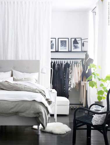 Un espace dressing est crée avec des rideaux blancs dans cette chambre parentale. Avec portant de vêtement et la lampe murale en acier noir comme déco loft