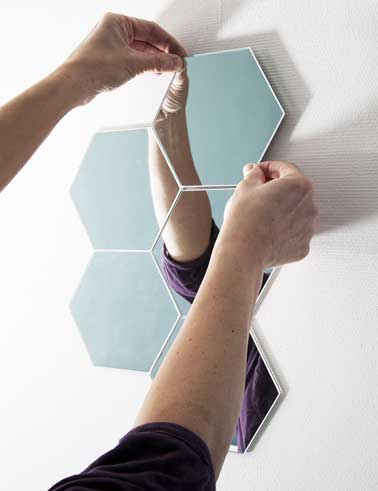 Chaque petits miroirs hexagonaux est fixés sur le mur un par un en suivant un modèle de forme géométrique dessiné au préalable contre le mur