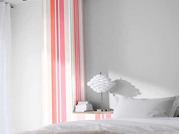 Un lé de papier peint à rayures taupe et rose pour une déco chambre contemporaine. Posé sur un seul pan de mur ce papier peint coloré habille la pièce blanche