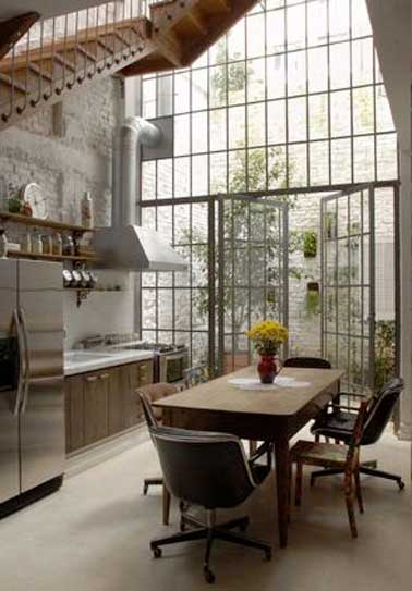 On mix les genres déco dans la cuisine avec sa grande verrière. Touches industrielles avec la hotte apparente et le mur en béton, notes rétro avec la table de cuisine et le meuble bas en bois