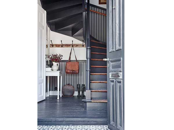 Avec son papier peint rayures et ses murs peints en gris anthracite, la cage d’escalier en colimaçon apporte du caractère à l’entrée. En accord avec le parquet repeint