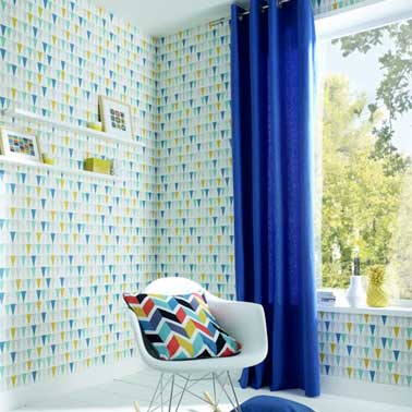 Un papier peint vintage inspiration scandinave à motifs bleu et jaune habille les murs du salon. Marié avec un rideau bleu et un coussin dessin géométrique