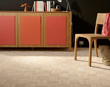 Un parquet massif en chêne est posé dans ce salon cosy. Il crée une douce harmonie de couleurs avec les meubles repeints en tons orange et la chaise en bois.