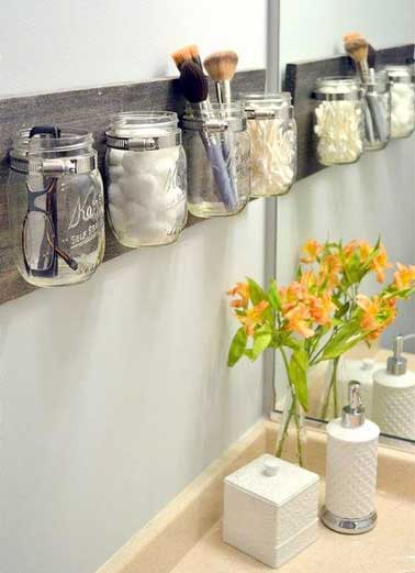 Astuce de rangement récup spécial petite salle de bain. Des pots de confitures en verre sont fixés au mur et détournés pour ranger les produits du quotidien