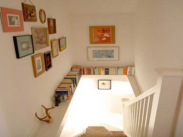 Dans cette cage d’escalier une poutre permet de créer une étagère pour le rangement des livres. Des cadres photos de toutes tailles colorent les murs blancs