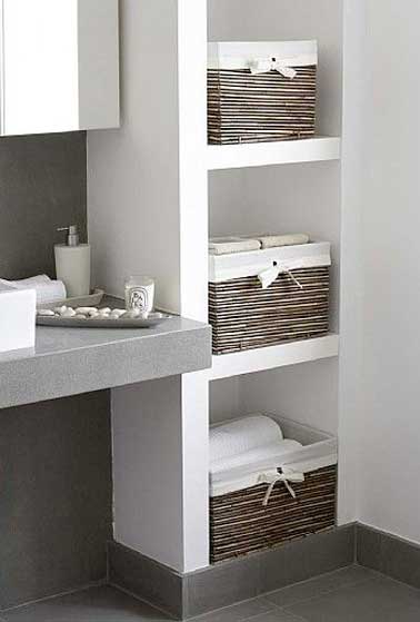 Un bloc de rangement est construit en carreaux de plâtre dans un mur de la salle de bain. Des paniers en osiers sur les étagères reçoivent le linge de bain