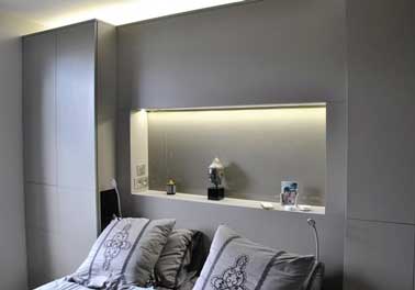 Tête de lit faite en coffrage bois entre deux placards dans une chambre grise. Avec ses led intégrés cette console pratique créée une ambiance cosy dans la pièce.