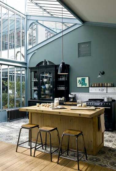 Une cuisine lumineuse avec sa verrière toit véranda. Espace structuré avec un sol en carreaux de ciment et déco loft pour l’îlot central et ses tabourets en bois 
