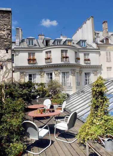 Un salon d'extérieur au charme urbain et cosy réalisé avec deux tables de jardin en fer et des chaises blanches design. Abrité du vis à vis par une végétation fournie il gagne en intimité