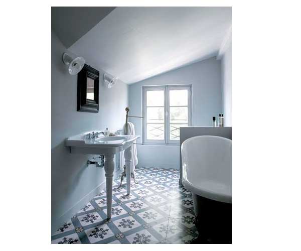 Une salle de bain sous toit avec des carreaux de ciment blancs et bleu harmonisé à la peinture bleu pastel des murs.