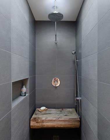 Douche à l’italienne ouverte réalisée en carrelage gris avec un banc en bois traité hydrofuge. Très fonctionnelle avec sa niche gain de place et sa colonne de douche pratique.