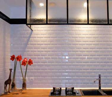 Cuisine style industrielle avec crédence en carrelage métro. Sublimé par une hotte verrière, un plan de travail en bois et des détails noirs sur l’électroménager et la frise murale.