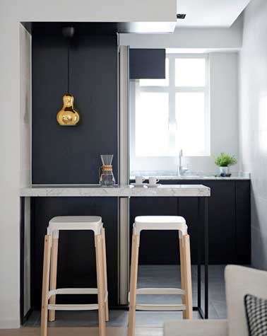 Petit coin repas avec plateau en marbre posé sur deux pieds en fer noir. Complété par des chaises bar en bois et plastique blanc et une suspension dorée, il fait la déco design de la cuisine