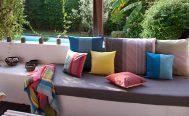 Plaid Surfing et mlx de coussins coloris Zanzibar, Luz Atlantique, Luz Limonade, Luz Garance, Luz céladon et Rhune donnent leurs couleurs à une terrasse de jardin ensoleillée. Tissage de Luz