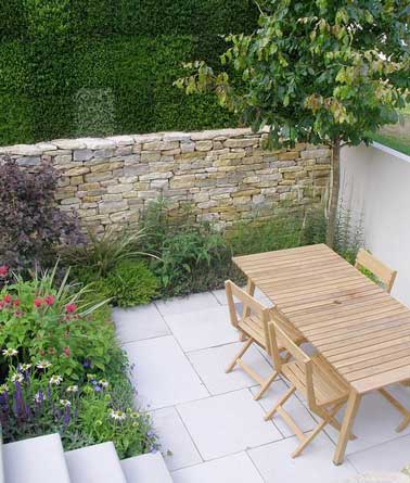 Sol en dalle de béton moderne et mur de clôture en pierre pour la petite terrasse d’un mas provençale. Isolée sans être fermée, elle accueille ses hôtes autour d'une table en bois 