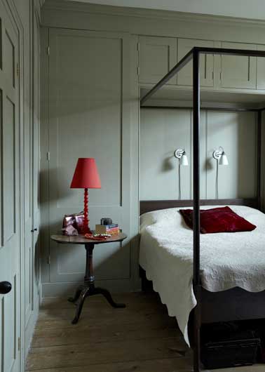 Chambre lumineuse avec couleur de peinture vert pastel sur murs et boiseries. Associée à un lit baldaquin noir et une lampe de chevet rouge. Peinture Farrow&Ball