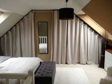 Poser des rideaux pour fermer le dressing sous pente ajoute une ambiance cosy dans la chambre. Ici deux rideaux en toile blancs assortis à la moquette, linge de lit et au plafond peint