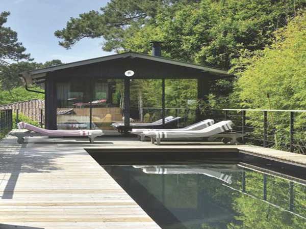 Terrasse en bois décorée avec un style de jardin zen. Des massifs de bambou plantés autour de la piscine d’extérieur et des transats créent une ambiance apaisante.