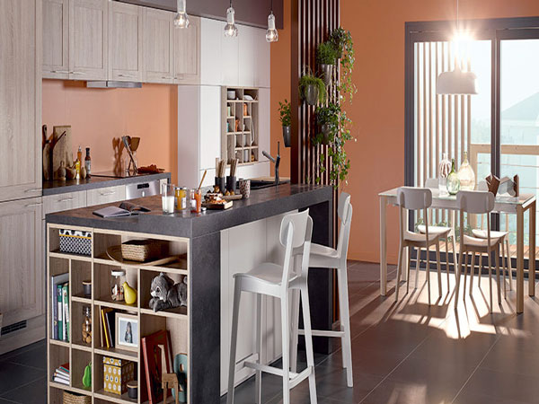 Cuisine américaine familiale aménagée avec un plan de travail anthracite prolongé d’une niche de rangement et des façades de meubles finition chêne clair et blanc mat.