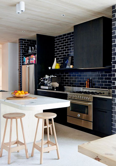 Jouez les contrastes de couleurs en associant un mur en brique noir sur la crédence de cuisine avec un sol carrelé blanc et un îlot central en marbre et réalisez une déco de cuisine tendance