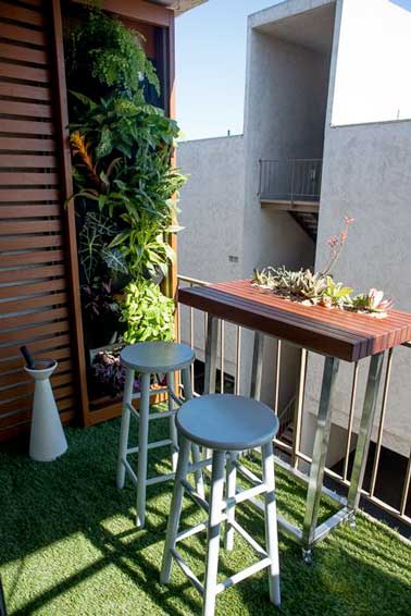 Séparation bois, mur végétal et sol gazon s’associent en camaïeux de couleurs pour structurer la déco de ce balcon. Table haute et tabourets blancs assortis