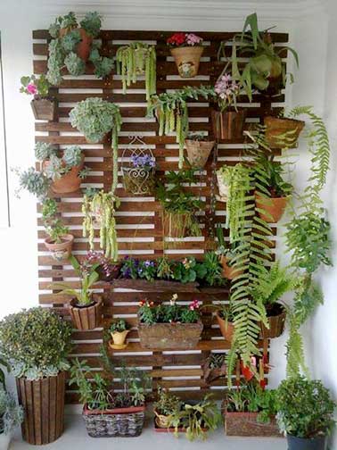 Mur végétal fabriqué avec des planches de palette. Démontées et fixées entre-elle elles sont ensuite vernies. Plantes en pots et jardinières sont fixées avec des crochets