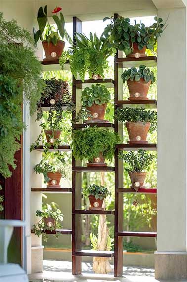 Un mur végétal sert de panneau de séparation extérieur dans un jardin. Construit avec des étagères en bois et des plantes grasses en pots il cloisonne l'espace sans l'étouffer