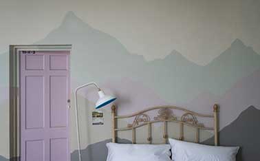 Peindre un décor avec des couleurs pastels dans la chambre Des nuances de peinture sont utilisées en camaïeux pour peindre un décor dans la chambre. Dessiné sur le mur contre le lit, ce décor fait aussi une tête de lit originale