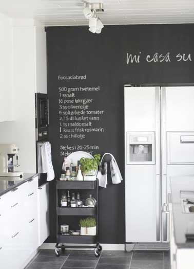 Mur peint avec une peinture tableau noir pour colorer la cuisine blanche. Coordonné avec la table roulante et le carrelage noir il valorise les meubles de cuisine blancs