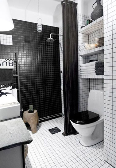 Ambiance design dans la petite salle de bain en carrelage noir et blanc. Douche à l'italienne à fleur de sol, porte-serviette échelle noir, pomme de douche inox et banc en bois brut coordonnés.
