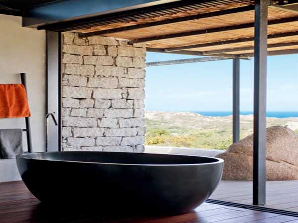 Une salle de bain zen installée derrière une baie vitrée avec vue panoramique sur la mer. Baignoire îlot en résine noire et parquet en bois exotiques sont les atouts majeur de cette déco